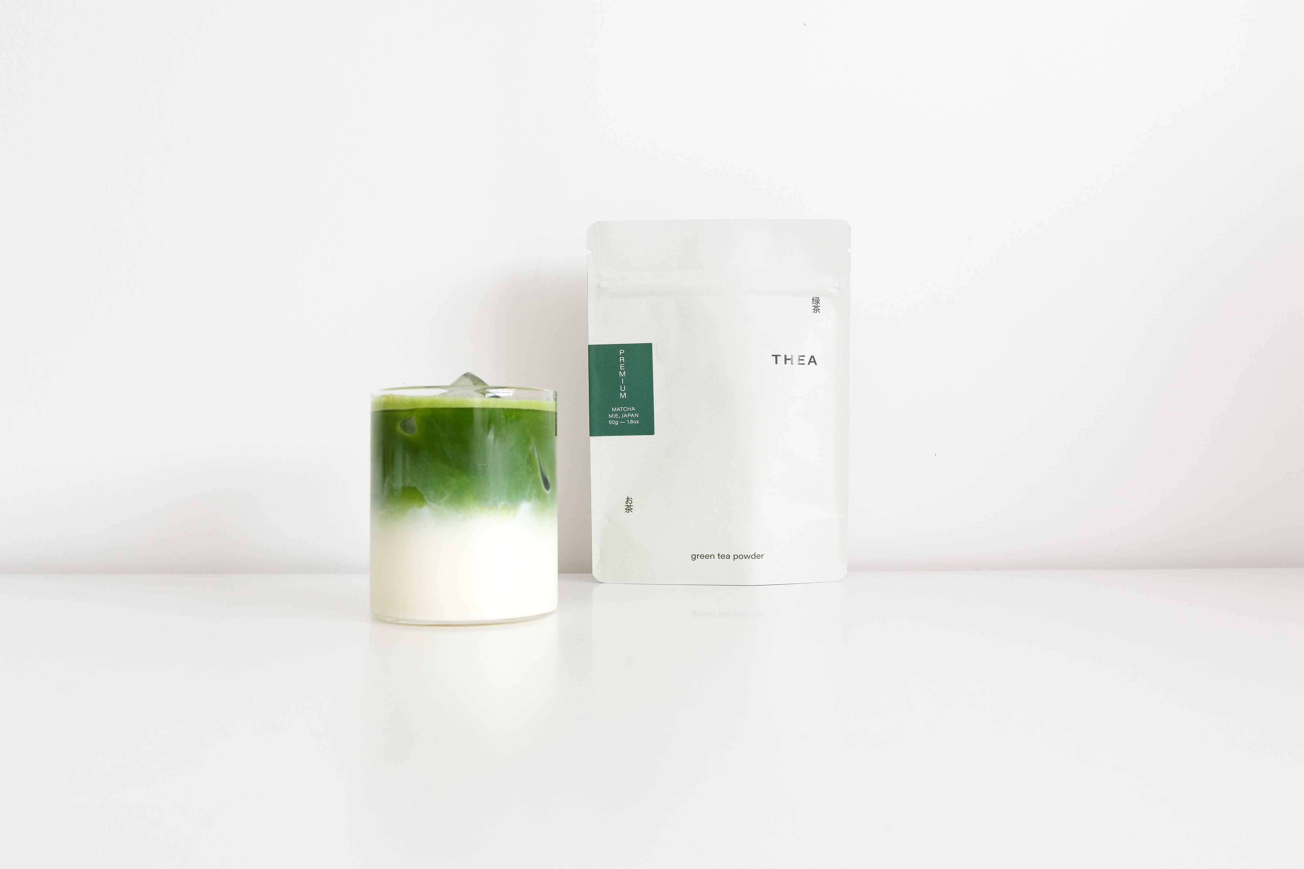 A matcha latte in a glass cup in front of a thea premium matcha pouch